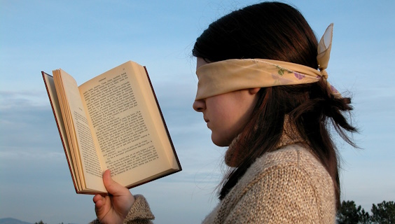 Kvinde med bind for øjnene holder bog op som for at læse